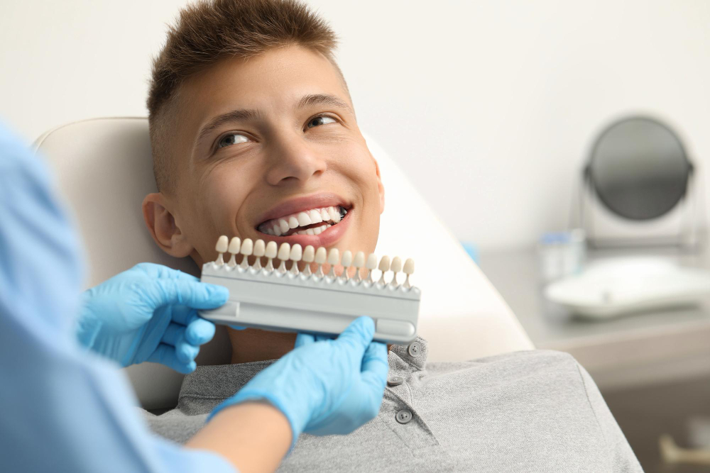 Dentist comparing a tooth shade guide with a patient's smile before teeth whitening or smile makeover treatment.